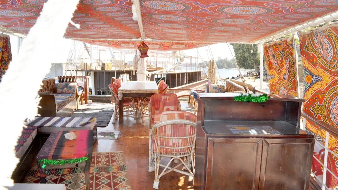 Upper deck of a traditional dahabiya boat with Egyptian decor and shaded seating area.