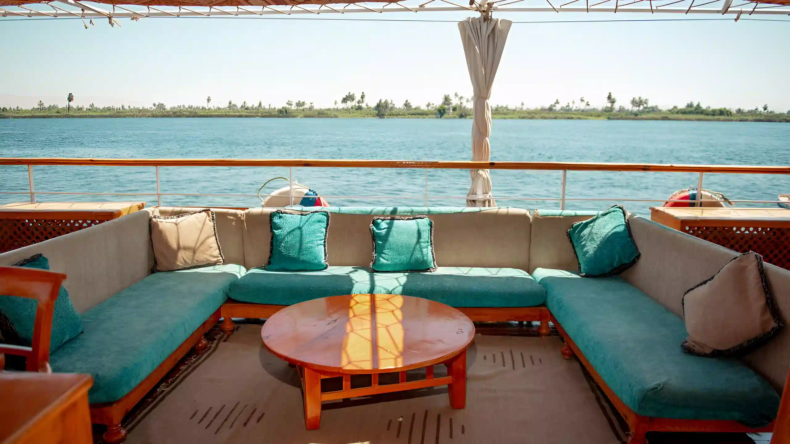 Outdoor lounge area on a dahabiya boat with turquoise cushions and Nile River view.
