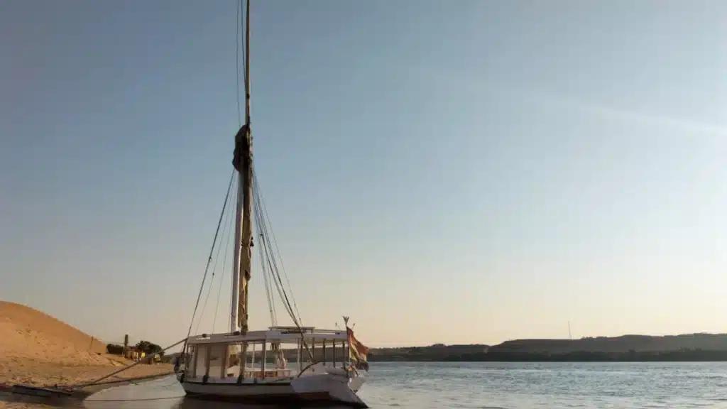 Traditional felucca moored along the Nile River near sandy desert dunes at sunset