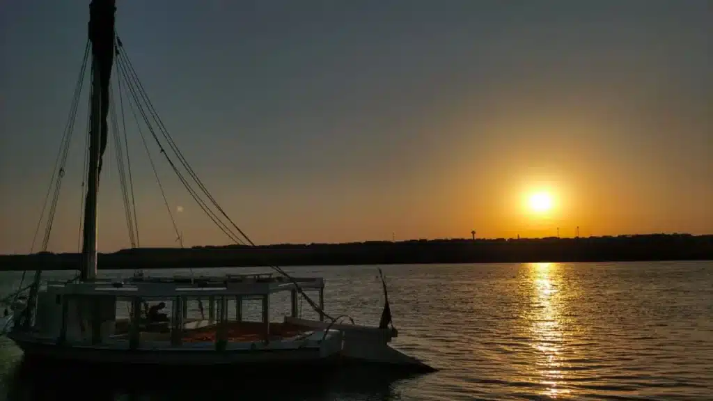 Traditional felucca boat silhouetted against a glowing sunset on the Nile River
