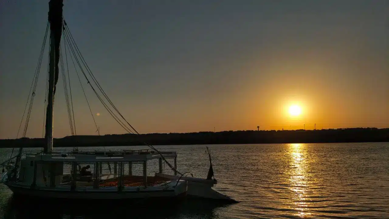 Traditional felucca boat silhouetted against a glowing sunset on the Nile River