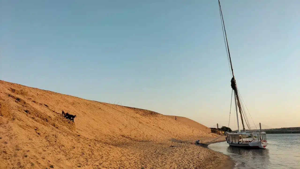 Felucca docked on the Nile shore beside a golden sand dune at sunset
