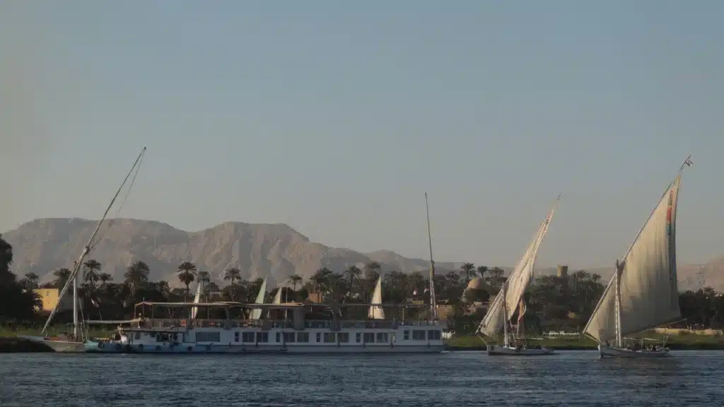 Traditional feluccas sailing on the Nile River with mountains and palm trees in the background
