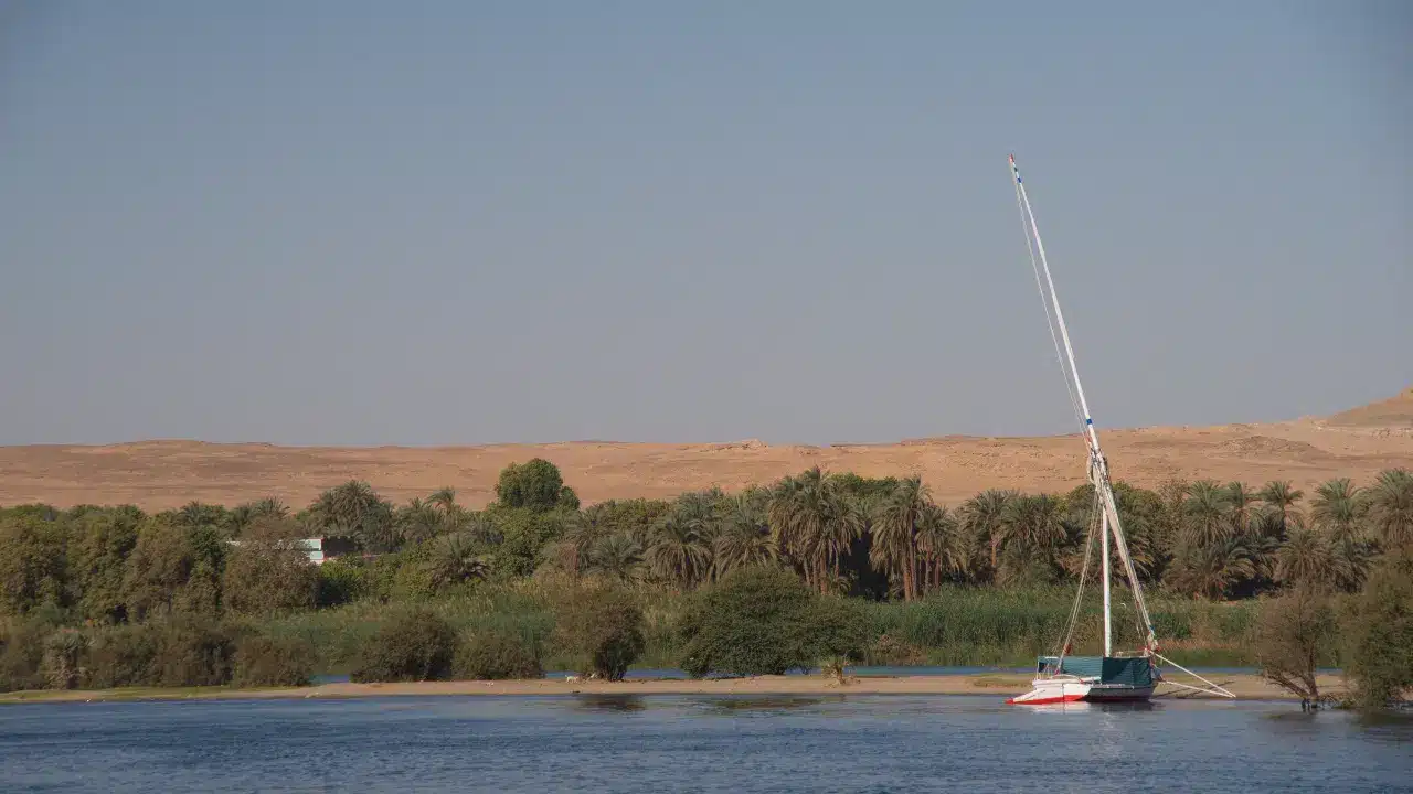 Traditional felucca moored by lush Nile riverbank with desert hills in Egypt