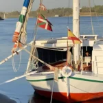 Traditional white sailboat moored on the Nile River, decorated with colourful flags from Spain and the Basque Country.