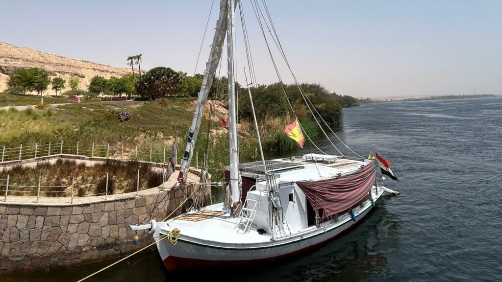 Felucca blanca con bandera española y egipcia amarrada en el río Nilo cerca de Asuán