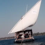 Dahabiya tradicional de vela latina navegando por el Nilo bajo un cielo azul despejado.