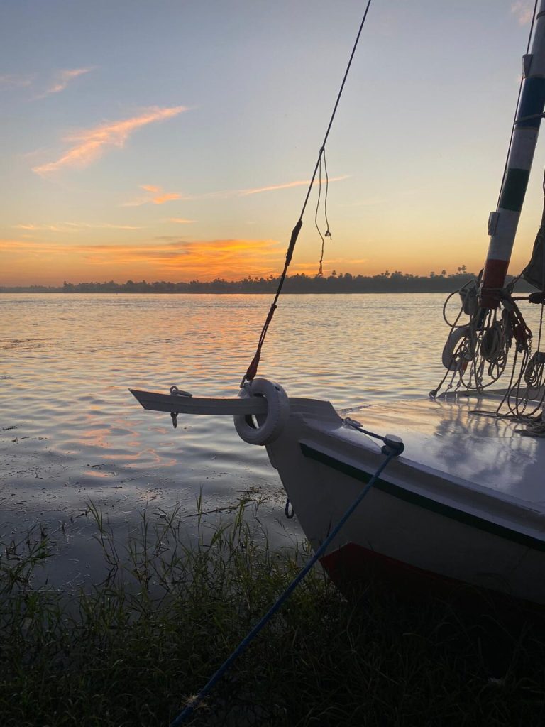 Bow of felucca Maitea at sunset on the Nile River in Aswan with warm sky and palm silhouettes