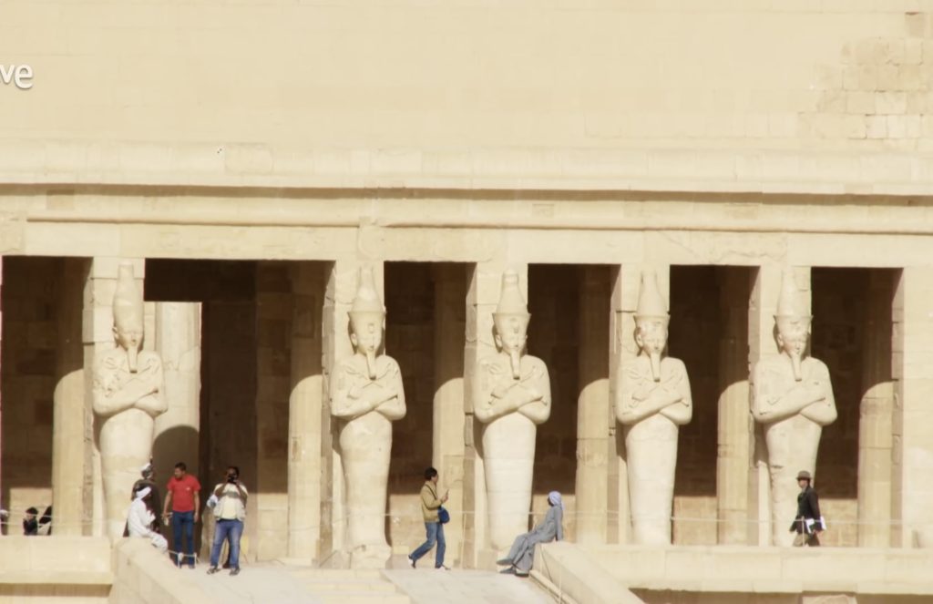 Osiride statues of Queen Hatshepsut at the Temple of Deir el Bahari in Luxor Egypt with visitors walking in front of the ancient columns