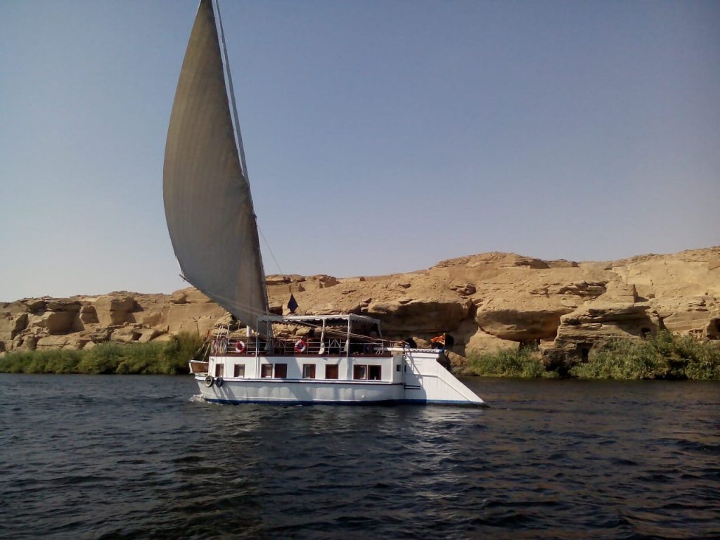 Traditional dahabiya sailing on the Nile River with desert cliffs in Upper Egypt